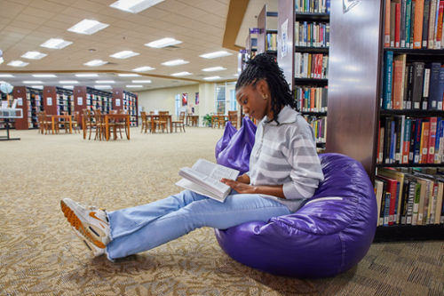 Female MGA student reads a book sitting on a bean bag chair in the Macon Campus Library. 